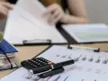 Kalkulator i długopis na dokumentach z wykresem. Osoba w tle przegląda papiery, przygotowując się do tego, jak rozliczyć PIT za wynajem mieszkania.