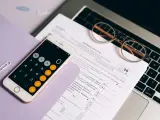 Telefon z kalkulatorem, okulary i dokumenty podatkowe na laptopie.
